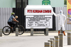 A cyclist rides by a fake coffin guarded by a mannequin dressed in protective gear in Kemang, South Jakarta, on Aug. 17. The display is part of a campaign to raise awareness about the dangers of COVID-19.  JP/Dhoni Setiawan