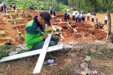 A grave digger writes the name of a deceased COVID-19 patient on a cross at Pondok Ranggon public cemetery, East Jakarta, on August. 31. 2020, while a burial proceeds in the background. Up to 40 people are buried in the cemetery every day. JP/P.J. Leo