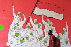 A man holding fishing equipment passes by a mural depicting medical workers on Jl. Raya Setu, Cipayung, East Jakarta on Sept. 7, 2020. More than 100 doctors have died from COVID-19 since the outbreak in the country started in March. JP/PJ Leo