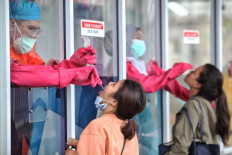 Medical staff take swab samples from two women at the Genomik Solidarita Indonesia (GSI) laboratory in Jakarta on Oct. 3. The government has set the price ceiling for individually requested COVID-19 swab tests at Rp 900,000 (US$60.60) to eliminate price disparities following concerns over the high cost of tests at private laboratories. JP/Seto Wardhana