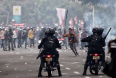 A protester runs toward police officers who stand guard on motorcycles during a clash in Jakarta on Oct. 13. A series of protests took place across the country following the House of Representatives&rsquo; decision to pass the jobs creation bill into law on Oct. 5. JP/Seto Wardhana