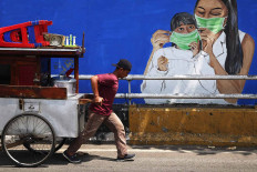 A chicken porridge vendor pulls his cart past a COVID-19 mural on Jl. KH Abdullah Syafei in South Jakarta on Nov. 16. The number of confirmed COVID-19 cases soared after many celebrated a long weekend from Oct. 28 to Nov. 1. JP/P.J. Leo