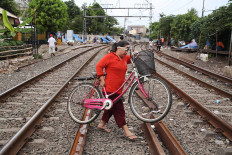 A woman carries her bicycle across railway tracks in Kramat, Central Jakarta, on Nov. 30. Because railway lines are not separated from residential areas, people often cross the tracks, thereby endangering their lives. JP/P.J. Leo