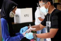 A poll worker (right) helps a woman put on a plastic glove before she casts her ballot at a polling station in Tapos, Depok, West Java, on Dec. 9. Poll workers enforced strict health protocols on voting day for the Depok mayoral election, requiring voters to wear gloves and face masks, among other precautions. JP/P.J. Leo