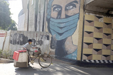 Life goes on: A food vendor pushes his laden bicycle past a coronavirus-themed mural of a health worker in Tebet, South Jakarta on Jan. 9, 2021. The prolonged pandemic does not affect people&rsquo;s spirit to remain active. (Courtesy of JADIGUNAImages/Jerry Adiguna)