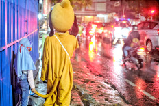 Soldiering on: A busker in an animal character costume shelters from the rain with his daughter along a busy street Jakarta on Jan. 26, 2021, in this color-monochrome photomontage. Indonesia reached 1 million COVID-19 cases on that day.(JP/Seto Wardhana)